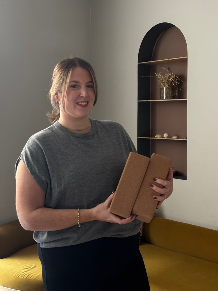 Ailbhe smiling, holding two yoga blocks, in the studio space.