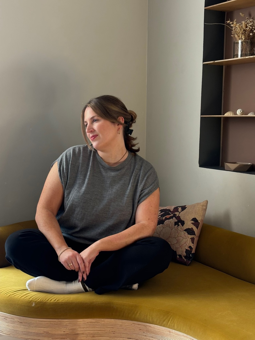 Ailbhe sitting cross-legged on a couch in the studio space, relaxed, soft light, small group setting.